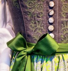 Närbild av en traditionell klänning med grönt band och broderade detaljer.