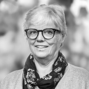 Kvinna med kort hår och glasögon bär en mönstrad scarf och ler.
