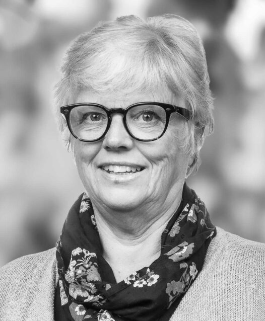 Kvinna med kort hår och glasögon bär en mönstrad scarf och ler.