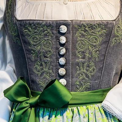 Närbild av en traditionell klänning med broderade detaljer och grön rosett.