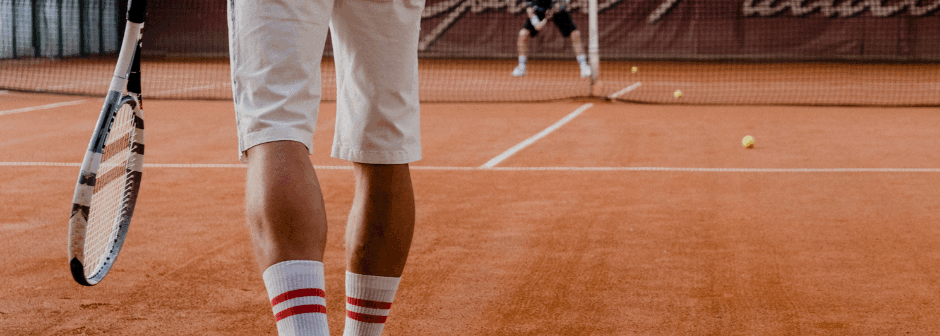 En person i vita kläder spelar tennis på en grusplan.