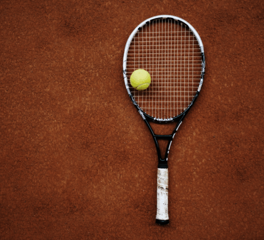 Tennisslagträ och boll ligger på en grusbana.