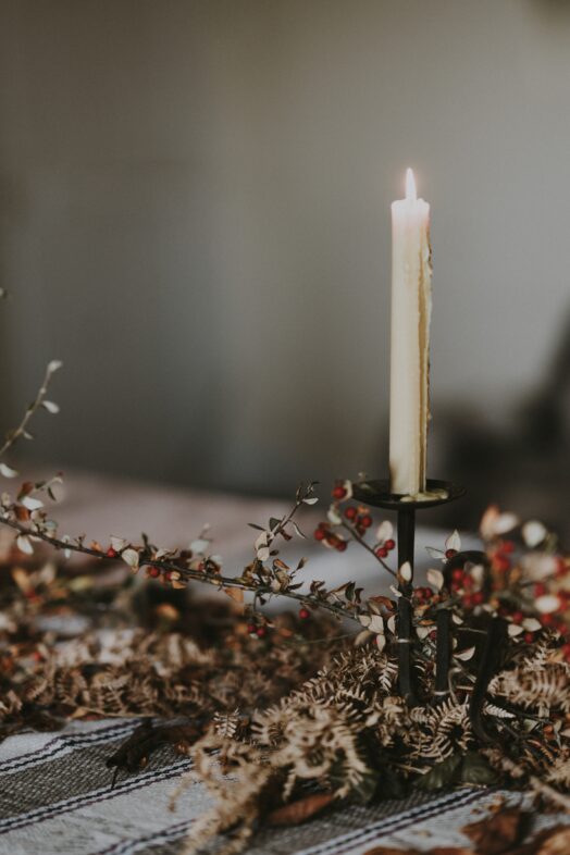Ett tänt stearinljus står på ett bord omgivet av torkade blommor.