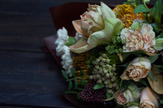 Bukett med olika blommor, inklusive rosor och gröna blad, på ett mörkt underlag.